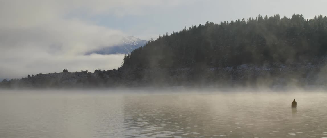 Morning mist rolling over a rippling lake with a forest and then a mountain in the distance