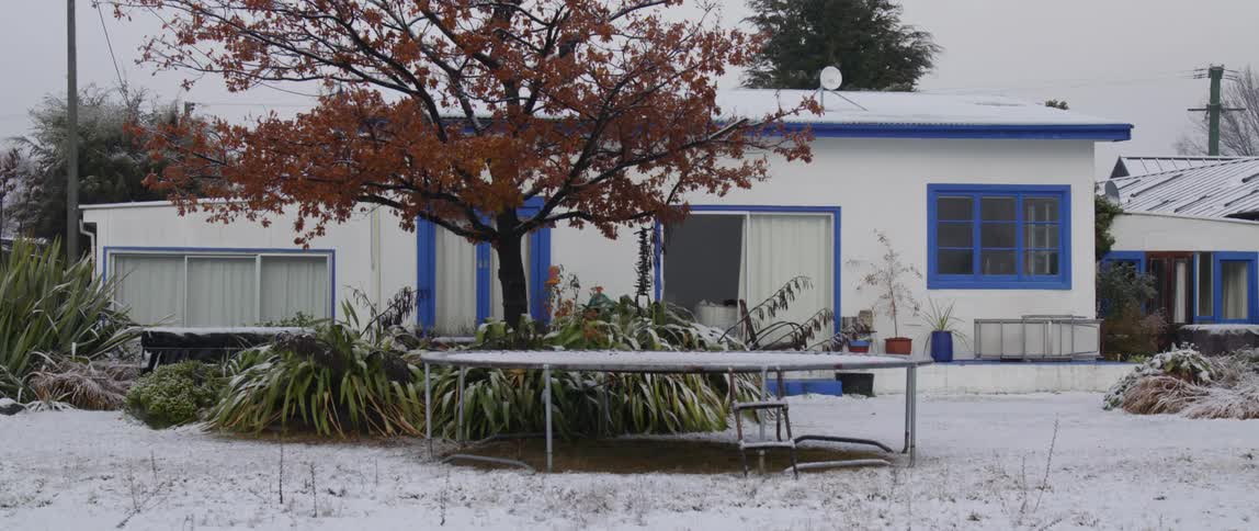 A white house with blue trim is seen from a backyard view during the winter