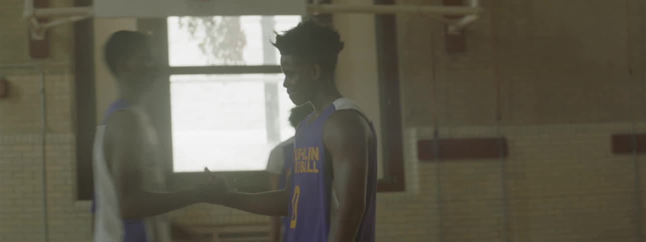 A boy walks on a basketball court and hugs another player