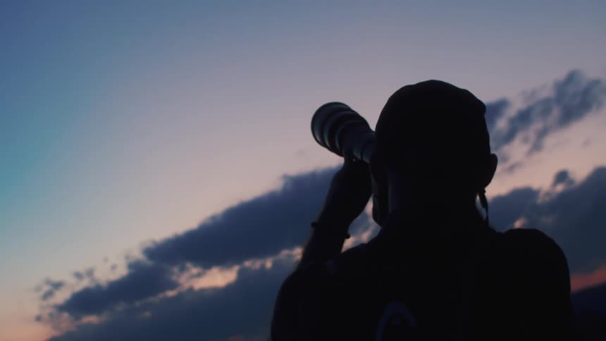 A man is standing outside holding a camera to his face as he takes pictures