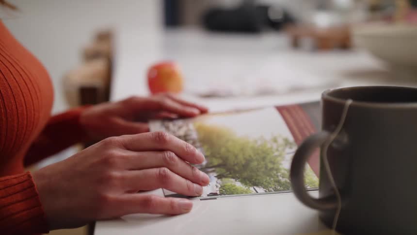 Woman with brown hair and red sweater leafs through magazine sitting at desk