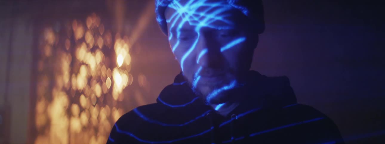Glowing lines made of light move across a mans face as he stands in a dark room