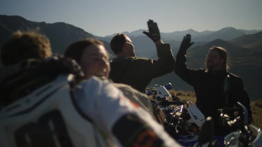 A group of motorcyclists high five while stopped on a mountain