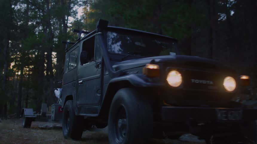 A jeep towing a motorcycle pulls off in the forest