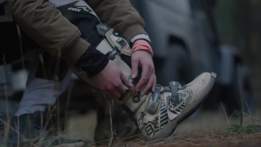 A girl tightens the straps on his boots while sitting behind his vehicle