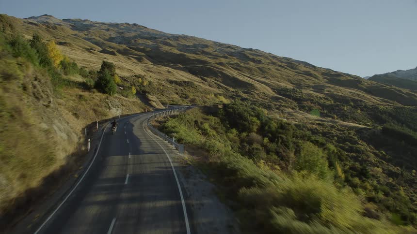 An aerial of a person riding a motorcycle on a road winding through hillsides