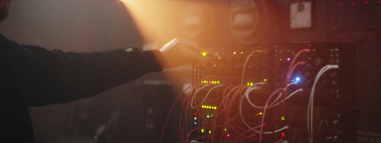 Man with beard and black shirt uses modular synthesizer