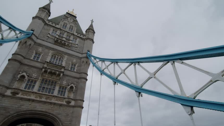 Blue struts lead to tower on bridge in city under an overcast sky