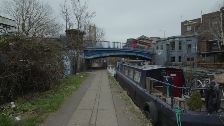 Moving alongside urban canal seeing a doubledecker bus on the overpass ahead