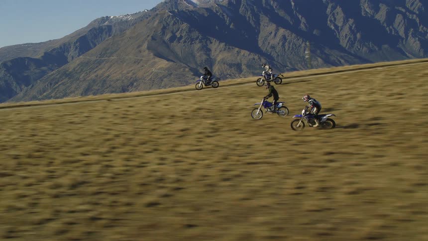 Four people ride motorbikes through a canyon