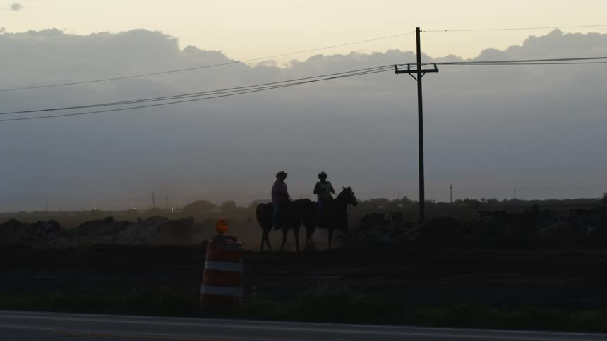 Cowboys ride in a rural area at sunset