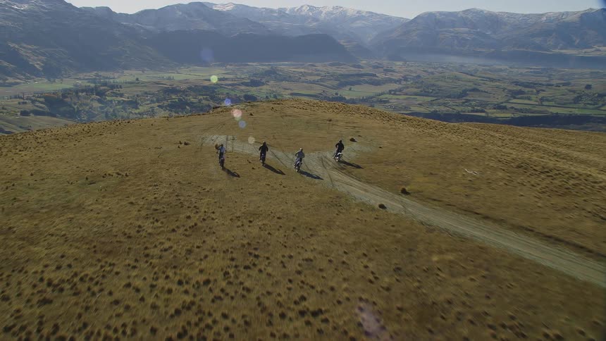 Four people on dirt bikes drive to the edge of a cliff
