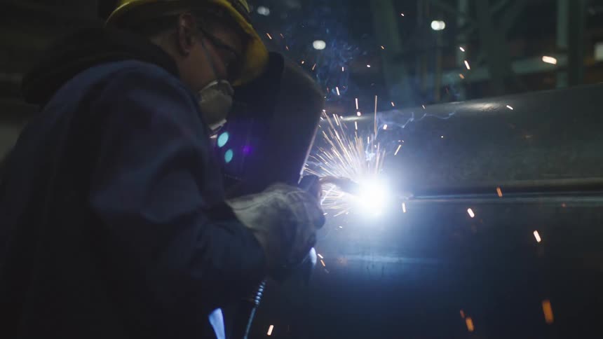Man wearing protective gear welds seam on tank