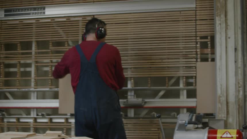 Man uses machine to cut boards while working in factory