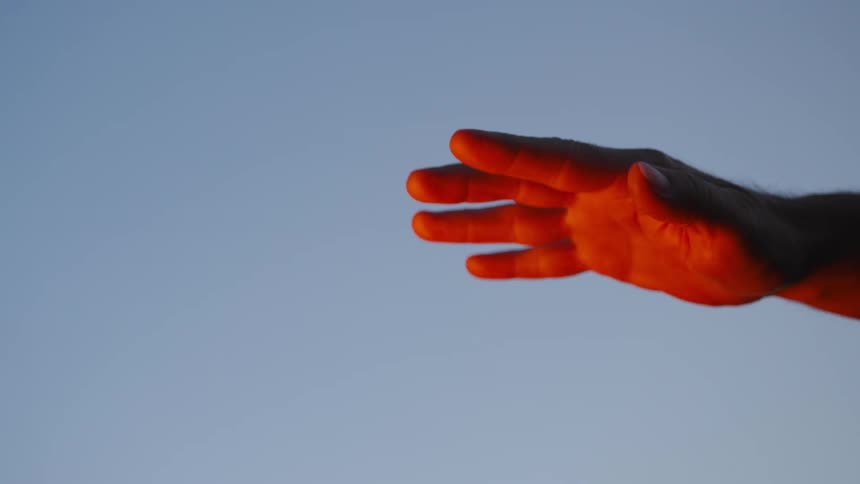 Red lighting reflects from palm of hand stretched out under clear sky