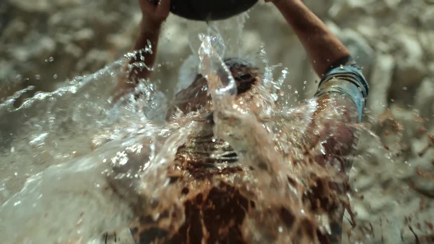 A man pours a bucket of water a mud onto his head