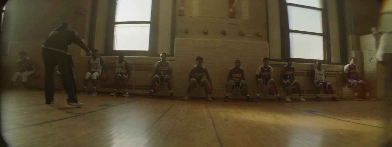 Players are seated and bouncing basketballs between their legs