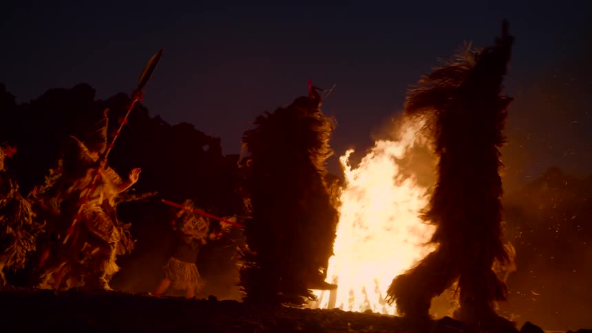 A group of people in costumes dance around a bonfire at nighttime