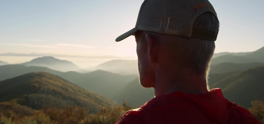 Back of the head of a man standing atop a mountain looking at the horizon at morning