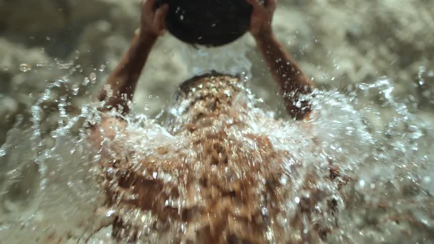 A young man is outside and is pouring a bucket of water on himself