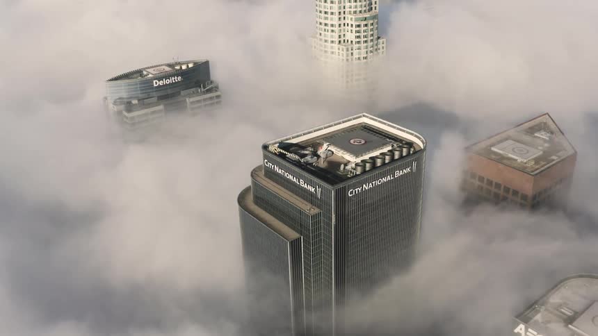 An aerial shot of tall buildings in a city with dense fog settled over the city streets