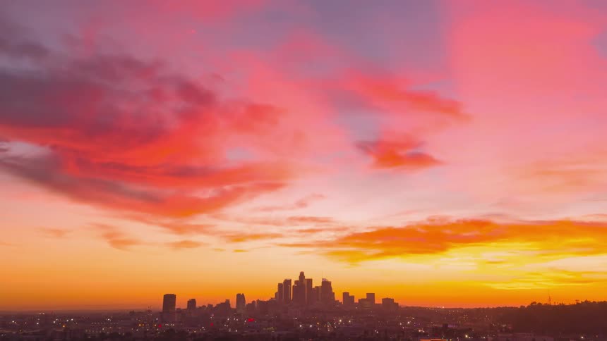 Moving toward a busy city as towers and buildings stand tall in the skyline and clouds move across a colorful sky
