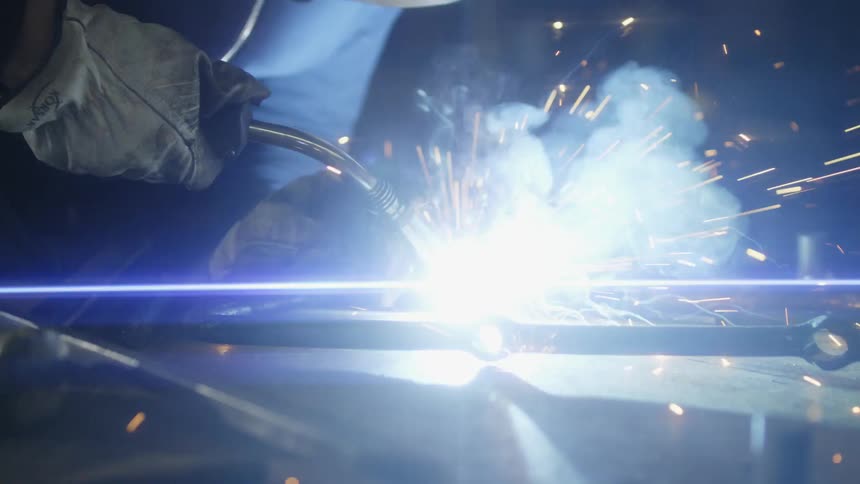 A welder wears protective gear while using a torch on metal