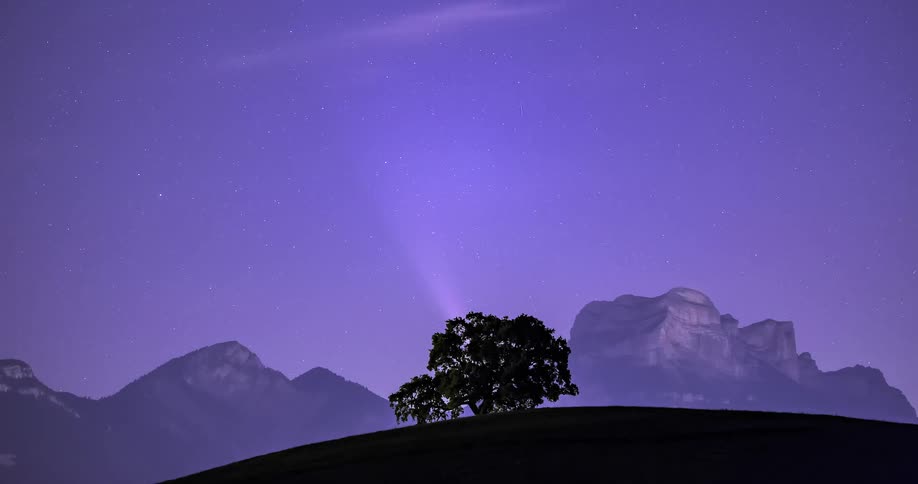 Time lapse of a comet moving behind the mountains behind the silhouette of a tree