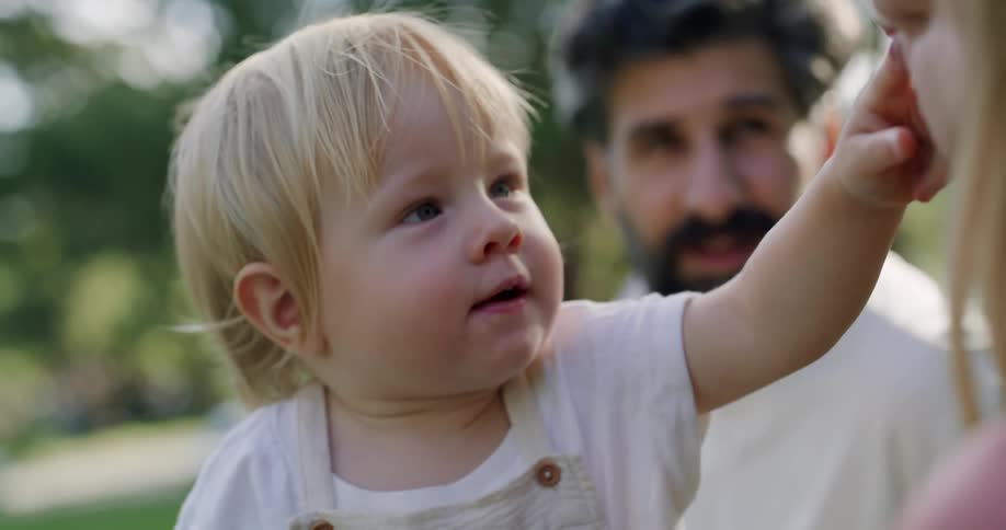 Baby touches mothers face next to father in the public park