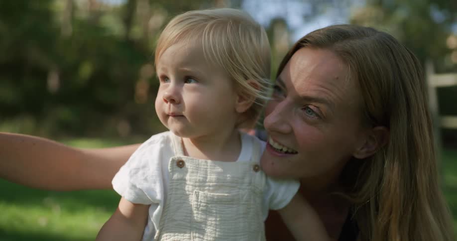 A mother plays with her toddler daughter outdoors in the yard during the day