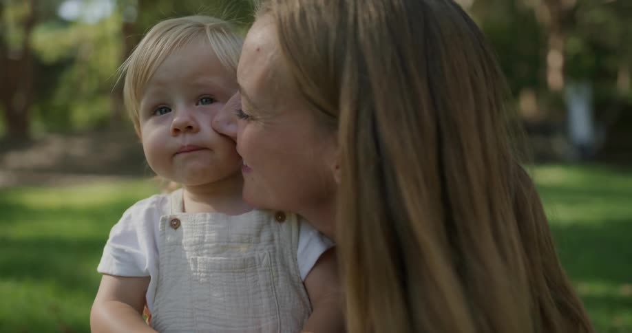 A mom kisses her toddler daughters cheek in the yard in daytime