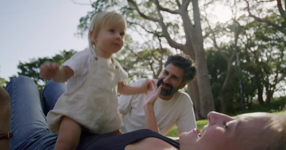 A baby bounces on his mother while she and the father are lying on the grass