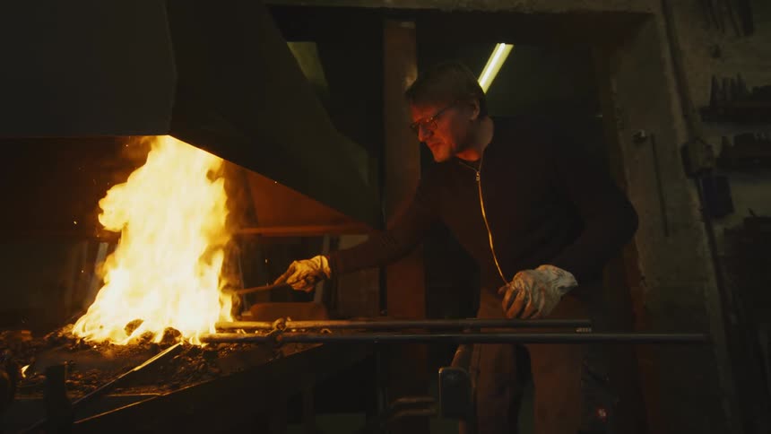 A metal worker in a factory works on a steel rod heated in a coal fire