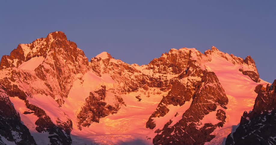 A time lapse of a snowy mountain range as the sun comes out over the mountains