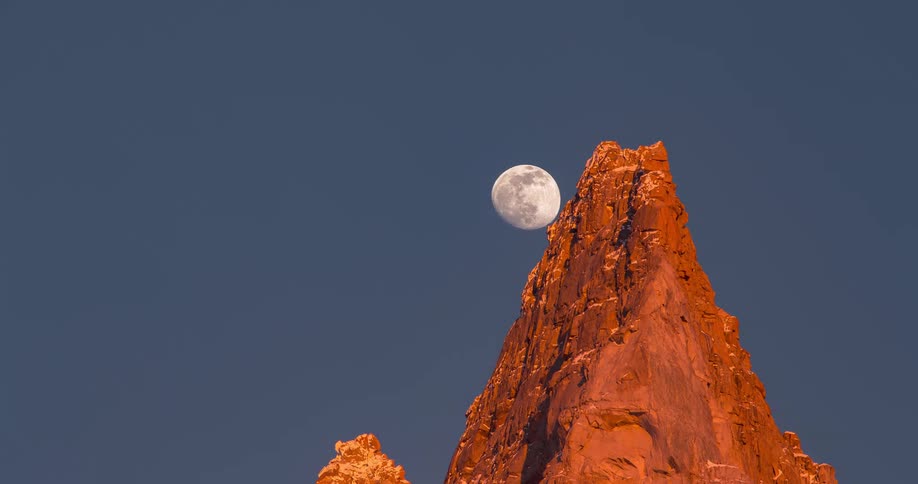 A time lapse of a pointy mountain peak with the moon rising up and over the peak