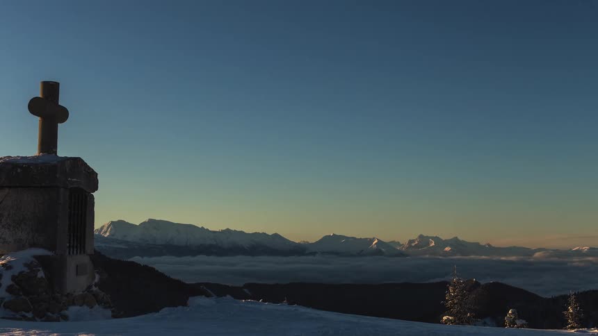A tomb and cross with snowy mountains in the distance at sunset