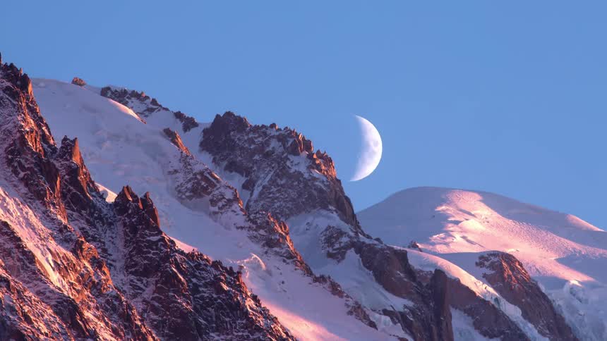 The moon passes over the mountains