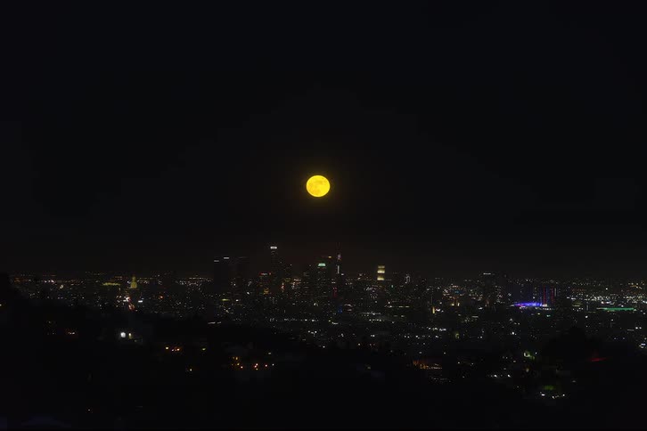 A time lapse of a city at night with a large orange full moon rising over the city