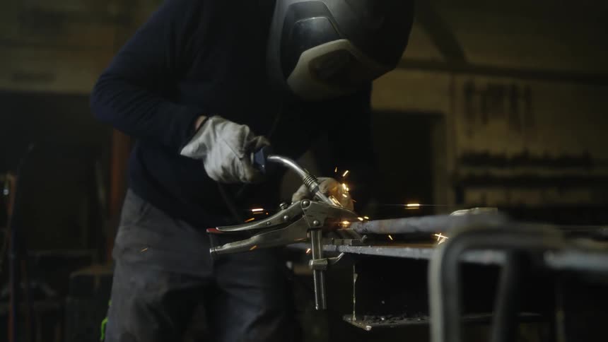 A man in welding protective gear in a workshop welding with sparks flying and arcs