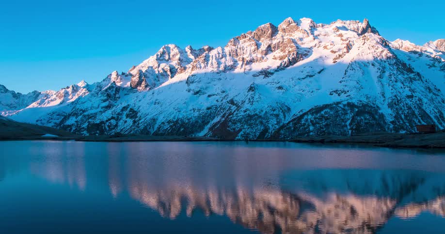 Time lapse of morning sunlight rolling over the slopes of a mountain close to a lake