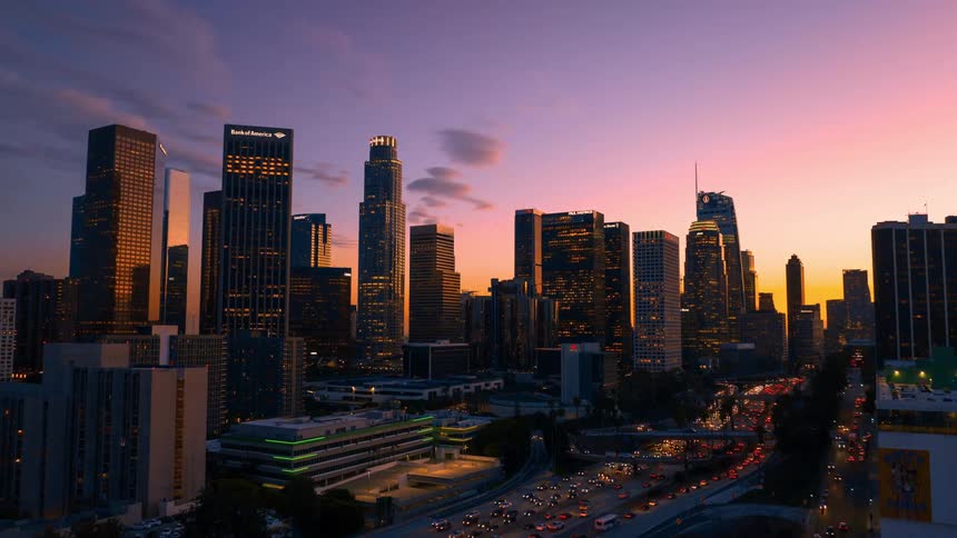 Lights on towers and skyscrapers glow in a busy metropolitan city as traffic fills the streets and clouds move across the sky as darkness falls