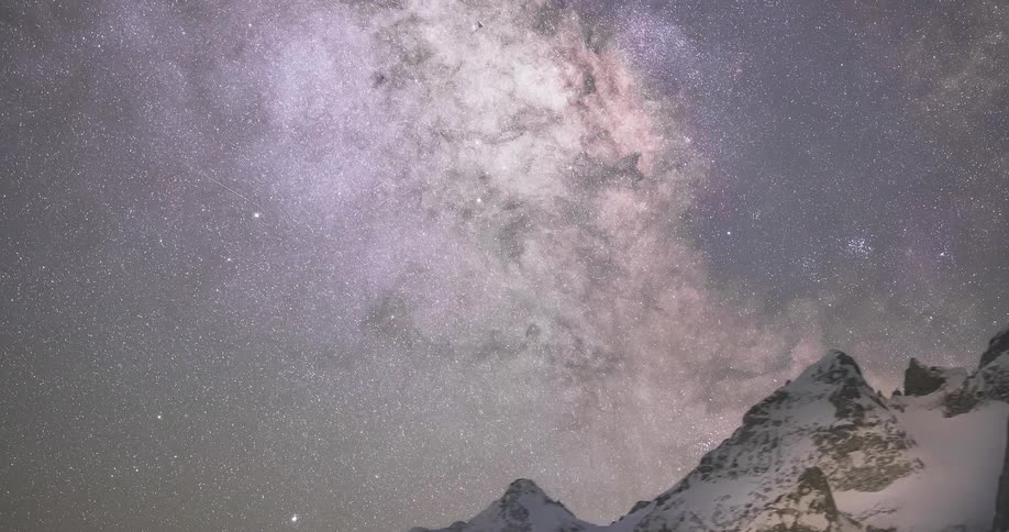 The top of a snow covered mountain is shown with the purplish night sky looking like a galaxy surrounded by stars