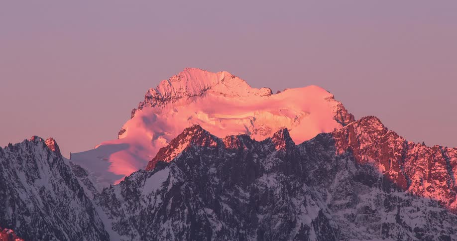 Time lapse of a mountain peak covered in snow changing colors during sunrise