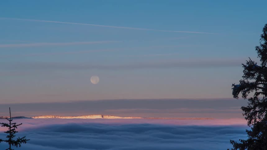 Clouds flow as moon sets during sunrise