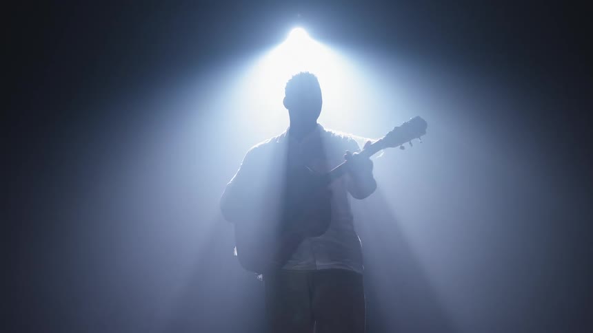 A man is playing a guitar under a spotlight