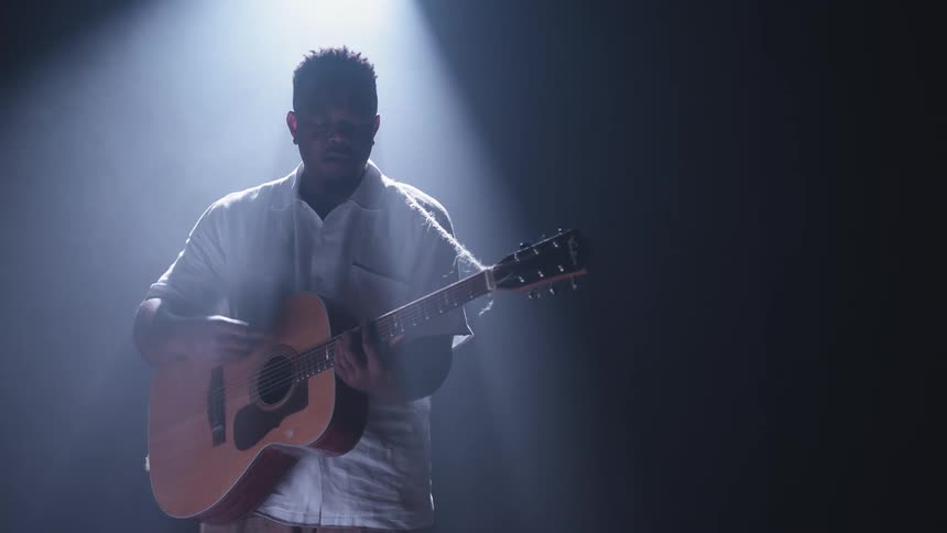A man is playing a guitar under a spotlight