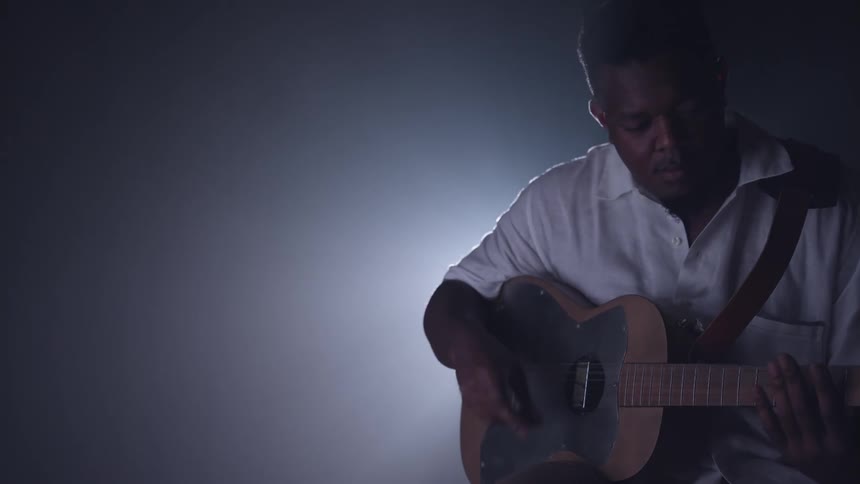Man plays a guitar with a light source right behind him