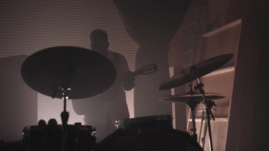 A man strums an acoustic guitar inside a studio