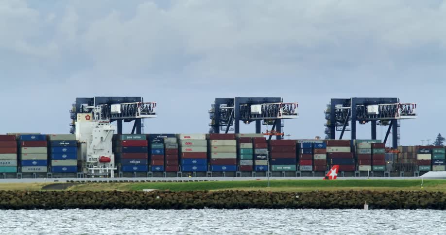 Shipping containers are stacked at the loading dock along the coast as a vehicle moves nearby