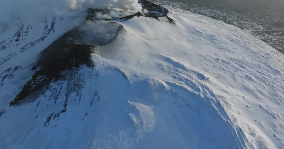 An enormous volcano is covered in snow as it releases steam and smoke